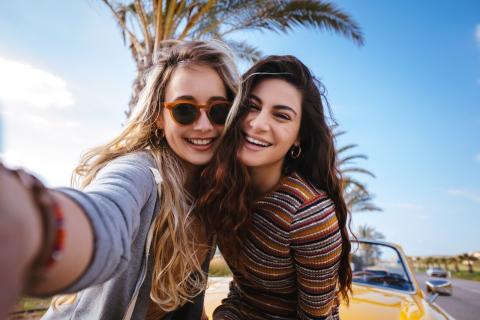 Two young women taking a selfie in front of a car and an open road