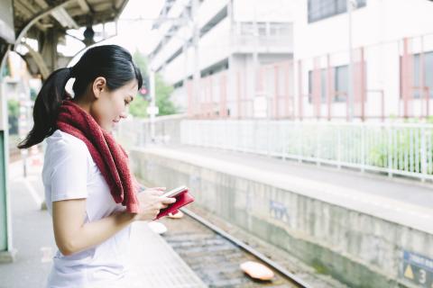 A woman waits on a train platform and looks at her phone