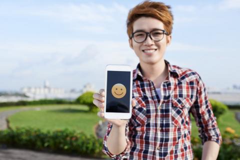 A woman holding a phone with a smiling emoji on the screen