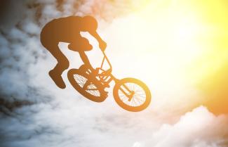 A bike rider doing a high jump against a cloudy sky