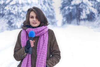 A presenter in a snowy landscape holding a microphone