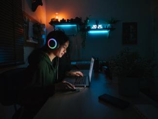 A female student uses a computer in a dark bedroom