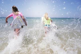 Two girls running into the sea carrying surfboards