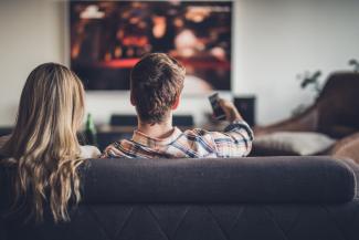 A teen boy and girl sit on a sofa watching a film