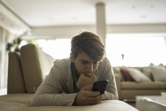 An teen boy looks at a phone with an anxious expression