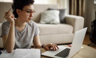 A woman holding a pencil and using a laptop