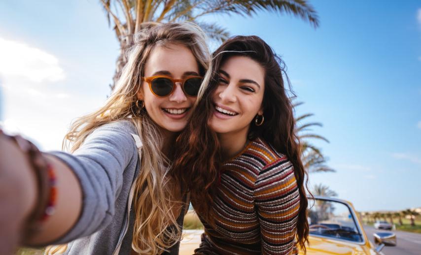 Two young women taking a selfie in front of a car and an open road