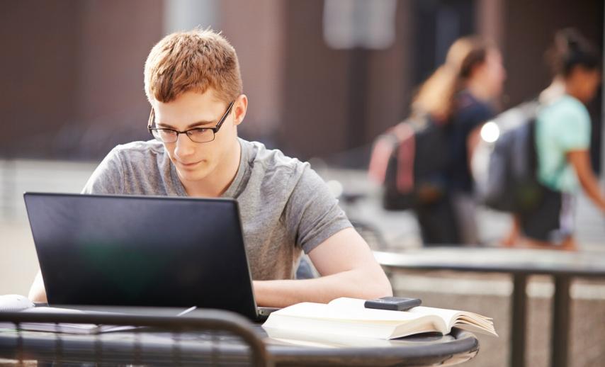 A student at an outdoor table looking at a laptop screen