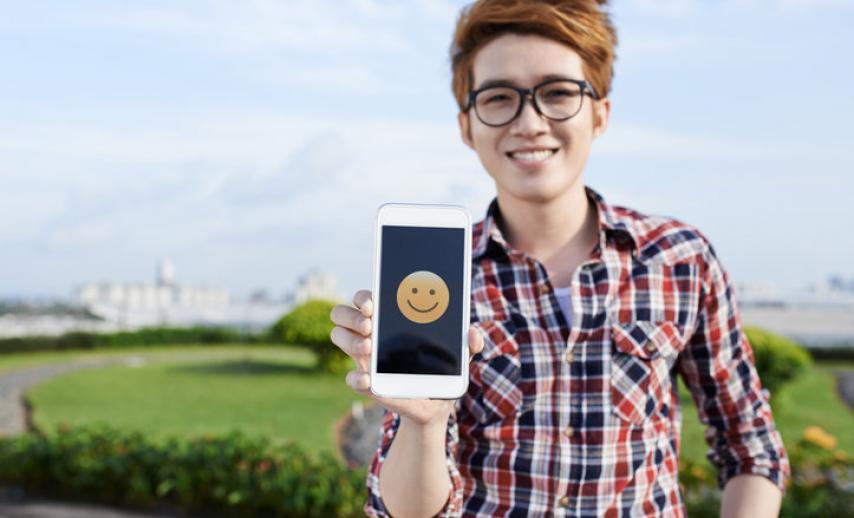 A woman holding a phone with a smiling emoji on the screen